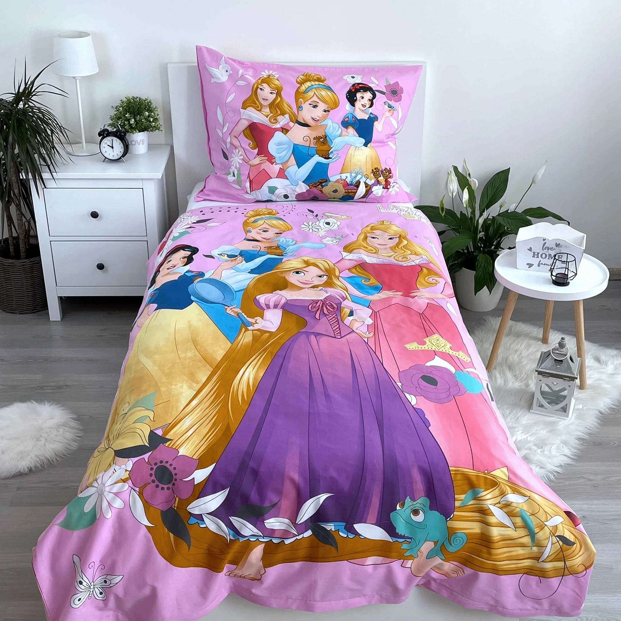 Ambiente-Aufnahme der Disney-Prinzessinnen-Kinderbettwäsche in einem weißen Bett; der rosa Deckenbezug zeigt großflächig Rapunzel, Schneewittchen, Cinderella und Aurora, während das passende Kopfkissen ordentlich am Kopfende platziert ist.