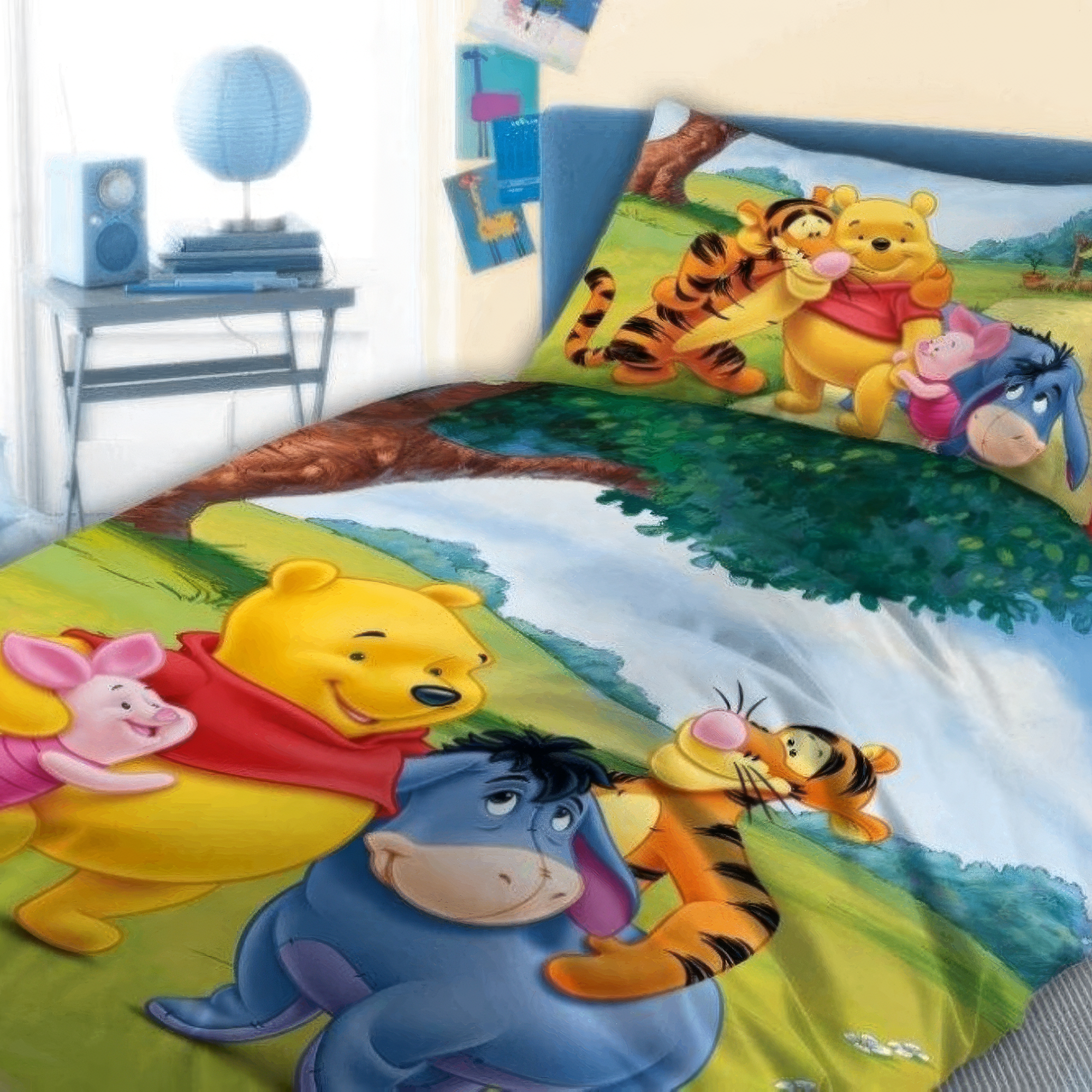 Perspektivische Ambiente-Aufnahme der Winnie-Pooh-Kinderbettwäsche; der farbenfrohe Deckenbezug zeigt Winnie Pooh, Tigger, I-Aah und Ferkel in einer grünen Landschaft, passend abgestimmt auf das Motiv des Kopfkissens im Hintergrund.