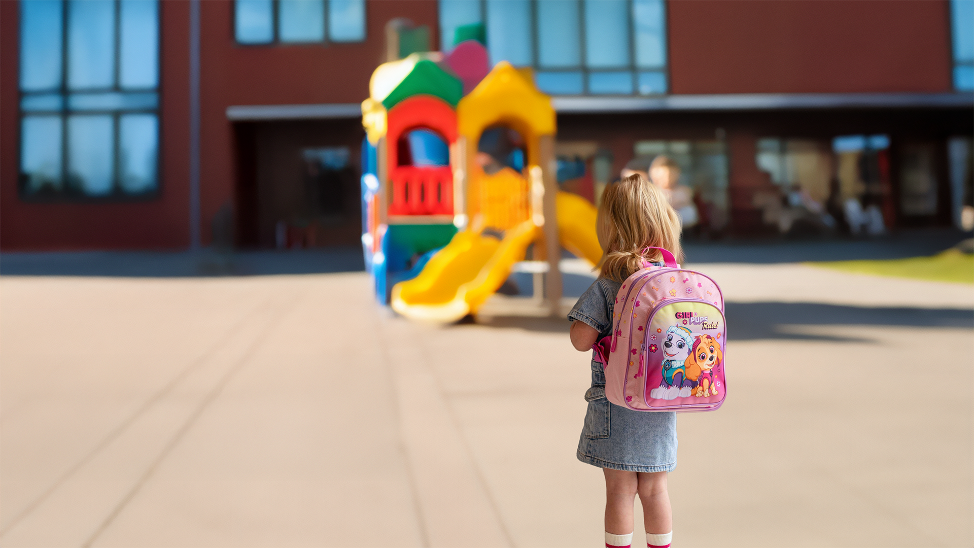 Kleines Mädchen mit rosa Paw Patrol Rucksack auf Schulhof vor buntem Klettergerüst – Lizenz-Kinderrucksäcke für Kindergarten und Schule