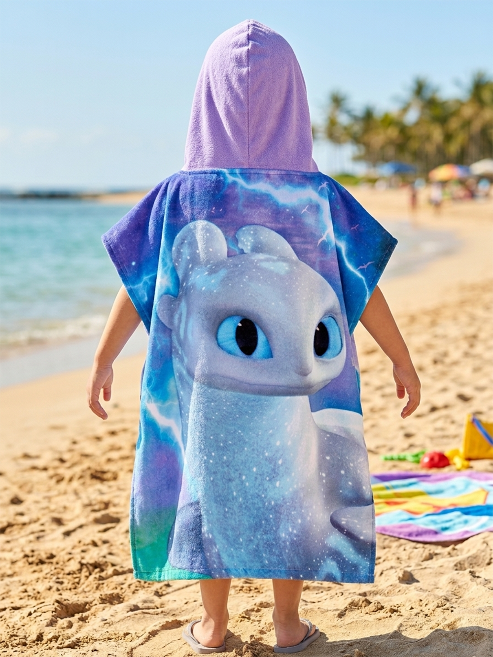 Mädchen präsentiert die Rückseite vom Dragons Badeponcho mit Kapuze 50x115 cm, 100% Baumwolle an einem Strand.