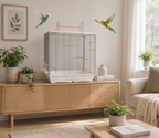 Eine helle und freundliche Wohnzimmerszene, in der das Vogelkäfig-Modell "Fiona" mit weißer Bodenschale und silbernem Gitter auf einem hölzernen Sideboard steht, während zwei Wellensittiche frei im Raum fliegen.