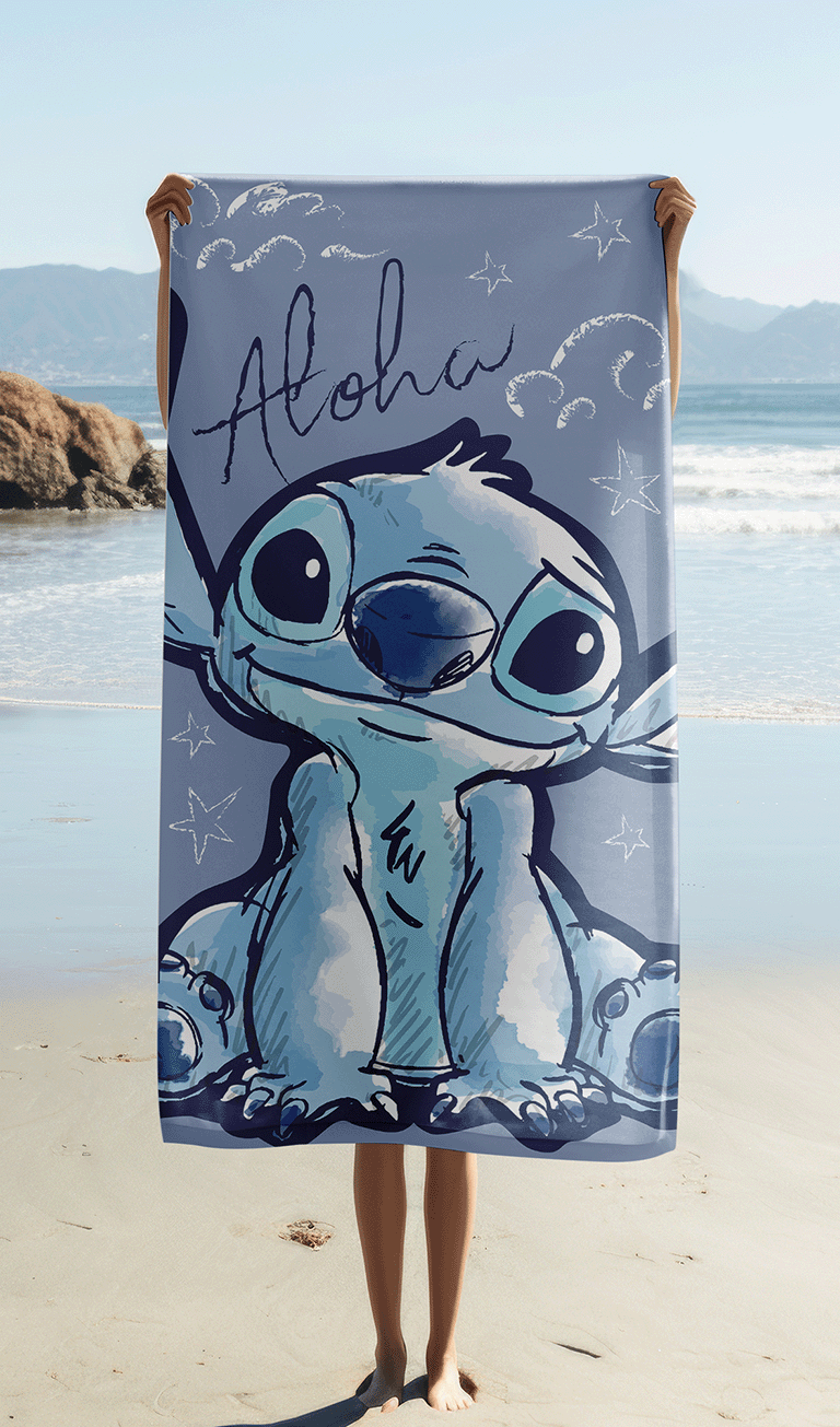 Das Stitch Strandtuch wird ausgebreitet vor einer Meereskulisse am Sandstrand hochgehalten, sodass das komplette Motiv mit dem gezeichneten Disney-Charakter perfekt sichtbar ist.