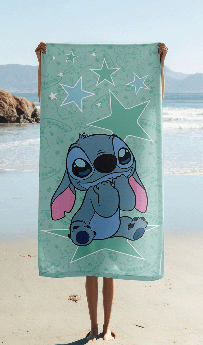 Das Stitch Strandtuch wird ausgebreitet vor einer Meereskulisse am Sandstrand hochgehalten, sodass das komplette Motiv mit Stitch auf dem Mond perfekt sichtbar ist.