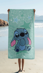 Das Stitch Strandtuch wird ausgebreitet vor einer Meereskulisse am Sandstrand hochgehalten, sodass das komplette Motiv mit Stitch auf dem Mond perfekt sichtbar ist.