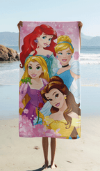 Das Disney Princess Strandtuch wird ausgebreitet vor einer Meereskulisse am Sandstrand hochgehalten, sodass das komplette Motiv mit den drei Prinzessinnen perfekt sichtbar ist.