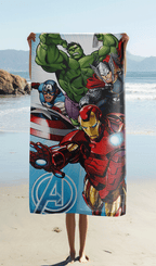 Das Marvel Avengers Strandtuch wird am Sandstrand hochgehalten, sodass das actionreiche Motiv mit den vier Superhelden und dem Avengers-Logo komplett sichtbar ist.