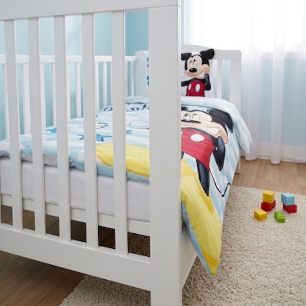 Kinderbett mit Mickey‑Bettwäsche, großem Mickey‑Motiv, blauem Muster und passendem Kissen. Spielblöcke auf Teppich, helles Kinderzimmer.