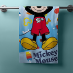 Frontansicht eines hellblauen Mickey‑Handtuchs am Stab. Mickeys Unterkörper mit roten Shorts und gelben Schuhen, bunte Sommer‑Icons und „Mickey Mouse“-Schriftzug.