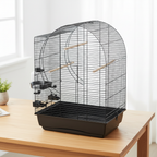 Leerer Vogelkäfig "Elizabeth" auf Holztisch, schwarze Gitter, weiße Basis, Holzstangen und seitliche Futterbehälter. Helles Zimmer mit Vorhang und Pflanze.