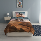 Frontansicht eines Motocross‑Bettwäsche‑Sets mit Fahrer im Sprung vor staubiger Landschaft. Kissen und Decke im passenden Dirtbike‑Design.
