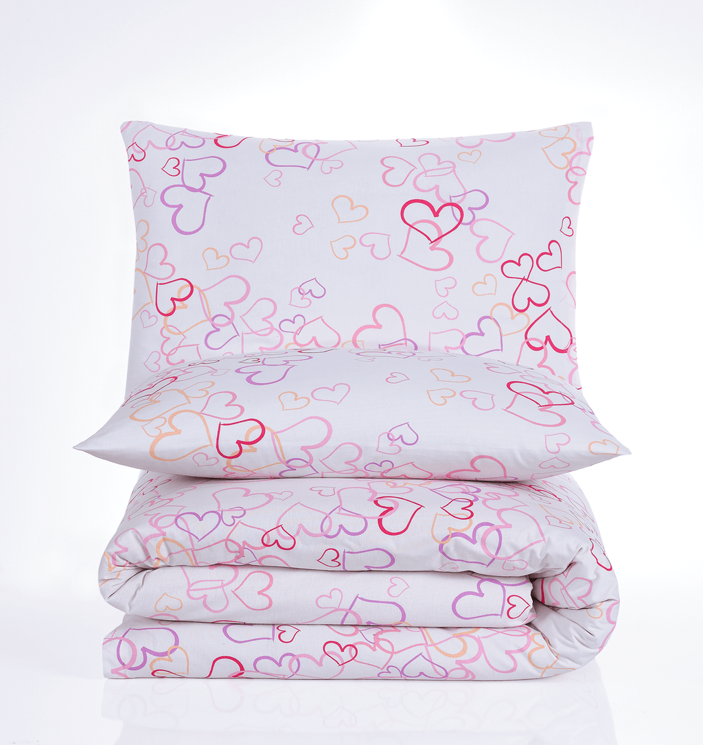 Gefaltetes Bettwäsche‑Set mit weißem Stoff und bunten Herzumrissen in Pink, Lila, Orange und Rot. Kissen und Decke im gleichen Muster.