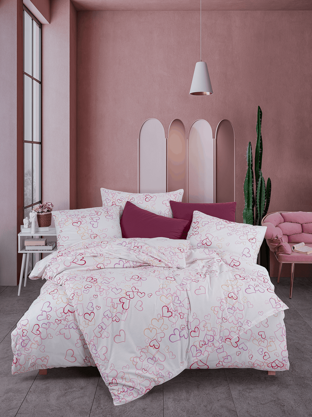 Bett mit weißer Herz‑Bettwäsche in Pink‑ und Rottönen. Modernes Zimmer mit rosa Wand, Deko‑Stuhl, Kaktus und hellem Tageslicht.