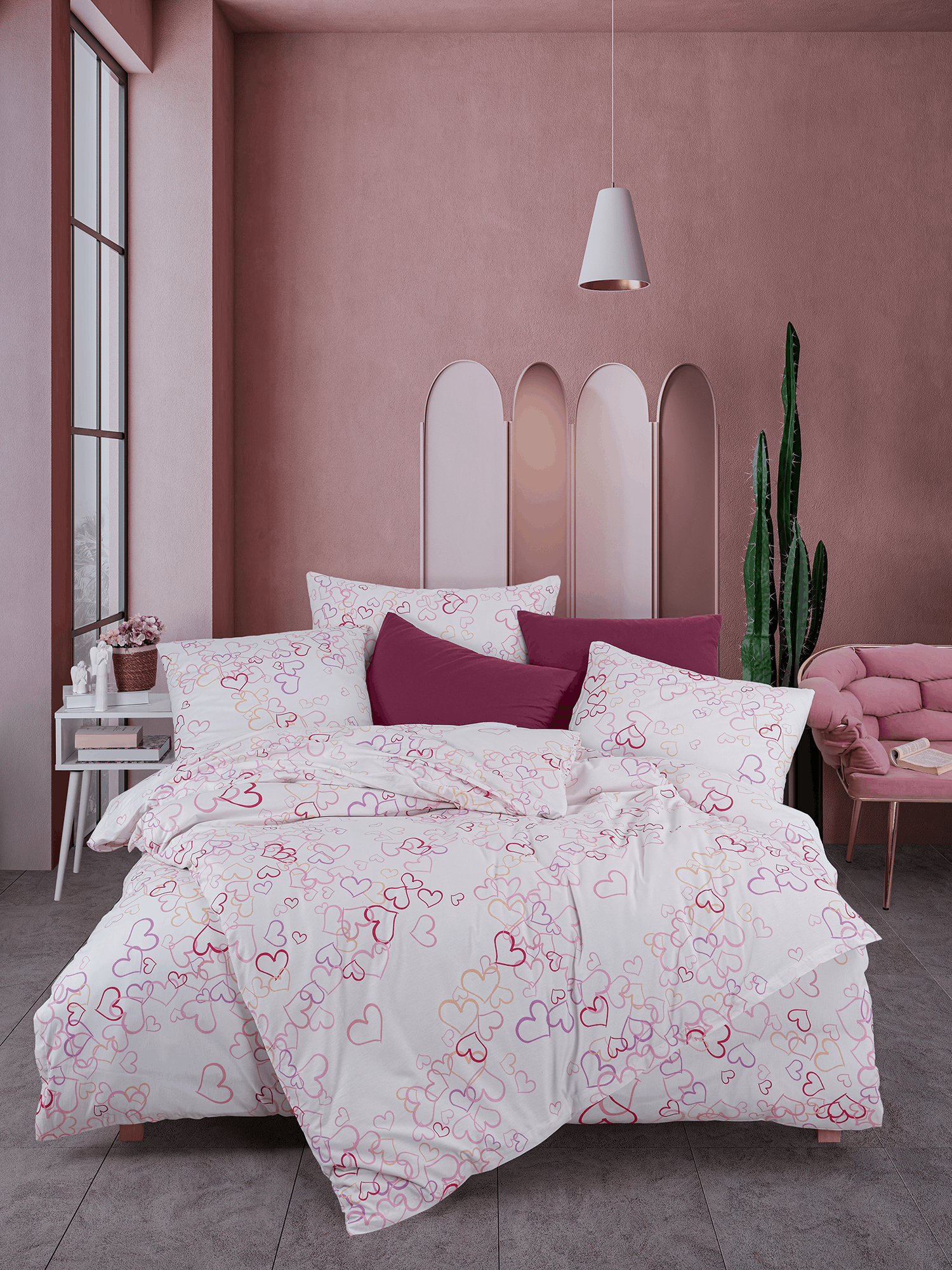 Bett mit weißer Herz‑Bettwäsche in Pink‑ und Rottönen. Modernes Zimmer mit rosa Wand, Deko‑Stuhl, Kaktus und hellem Tageslicht.