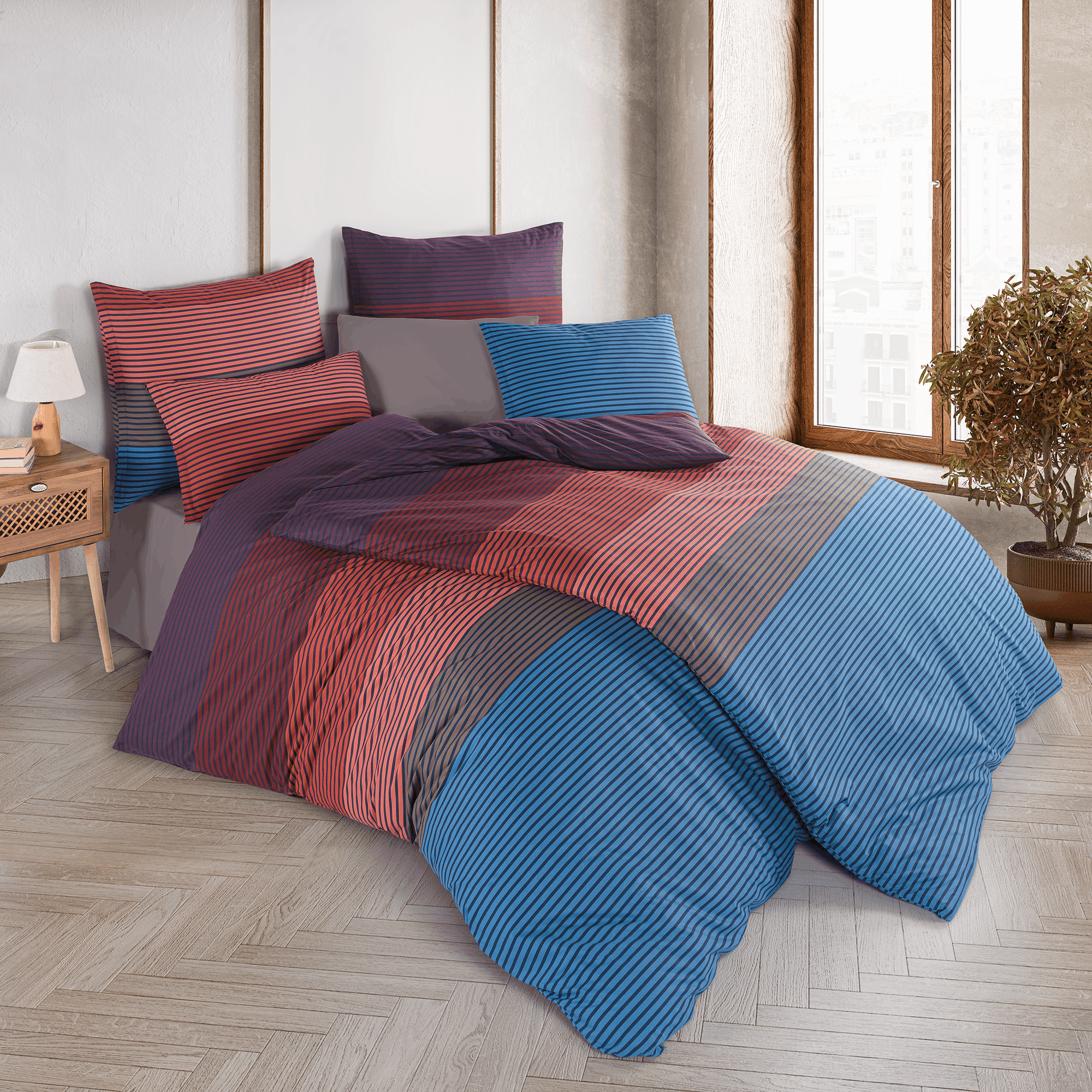 Gestreiftes Bettwäsche-Set komplett aufgezogen auf einem großen Bett in einem stilvollen Schlafzimmer mit Parkettboden; das Design zeigt ein feines, mehrfarbiges Streifenmuster in Blau, Rot und Violett.