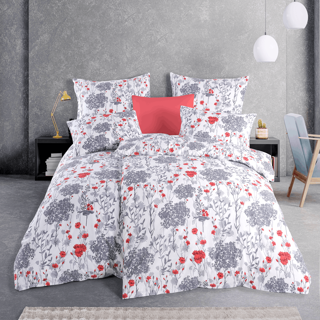 Bett mit weißer Blumen‑Bettwäsche in Grau und Rot. Modernes Zimmer mit grauer Wand, Hängelampen, Nachttisch und Deko‑Kissen.