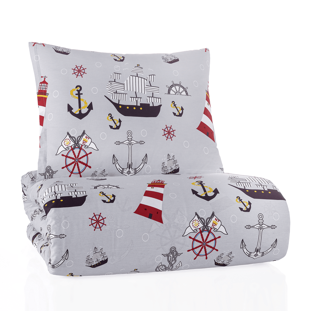 Zusammengefaltetes Bettwäsche-Set mit maritimem Motiv freigestellt auf weißem Hintergrund; Kissen und Decke zeigen rote Leuchttürme, dunkle Schiffe und Anker auf hellem Grau in kompakter Ansicht.