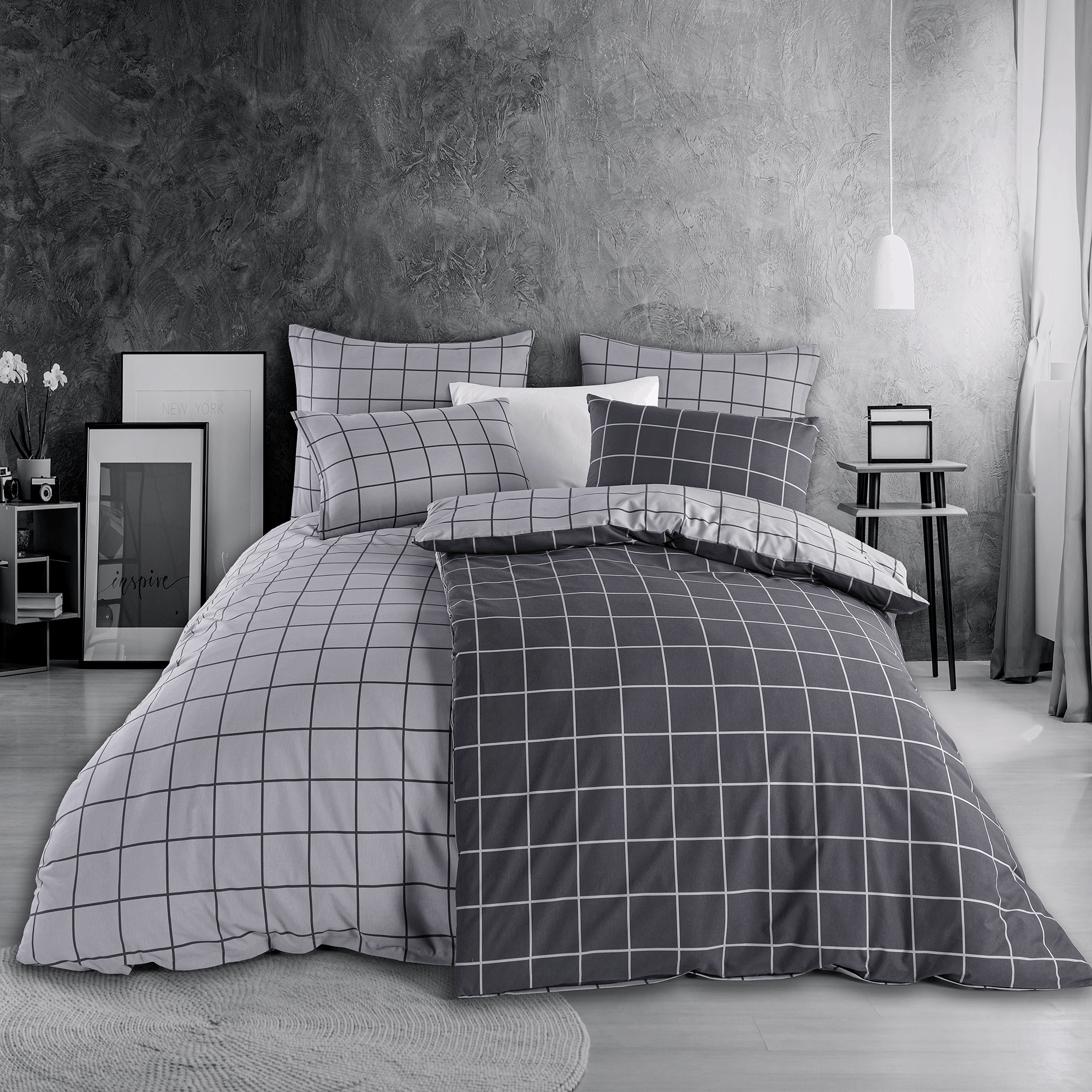Bett mit grauer Karo‑Bettwäsche in modernem Linienraster. Zimmer mit grauer Wand, Nachttisch, Lampe und minimalistischer Deko.