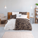 Bett mit zweifarbiger botanischer Bettwäsche in Dunkelbraun und Beige. Modernes Zimmer mit Holzregal, Pflanzen und warmen Akzenten.