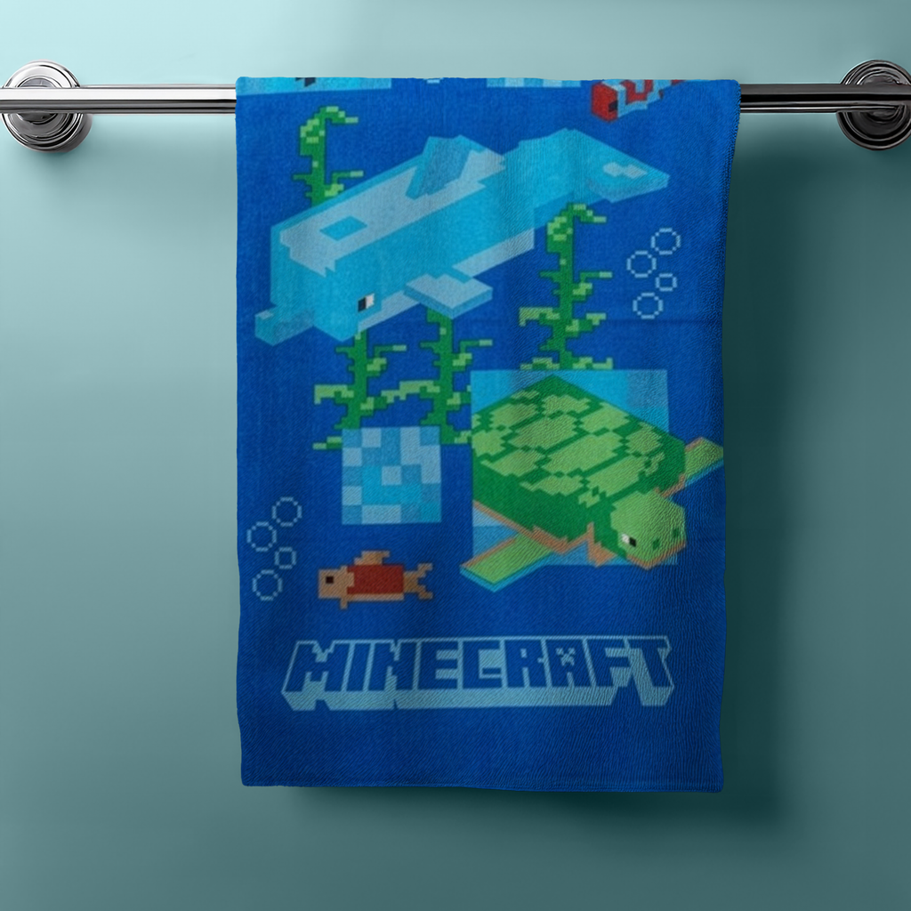 Hängendes blaues Handtuch mit Minecraft‑Unterwassermotiven: Delfin, Schildkröte, Fische, Seegras und Pixel‑Design. Unten Minecraft‑Logo.
