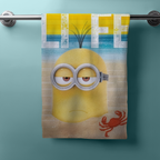 Hängendes Strandhandtuch mit Minion im Sand, Meer, Sonnenhimmel und kleinem roten Krebs. Oben großer „LIFE“ Schriftzug.