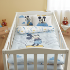 Babybett mit Mickey‑Bettwäsche. Vorderseite mit großem Mickey‑Motiv, Rückseite mit Mickey‑Kopf‑Muster. Kissen passend dazu. Helles Kinderzimmer.