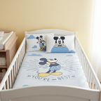 Babybett mit Mickey‑Bettwäsche: Vorderseite mit Mickey und Schriftzug. Zwei Mickey‑Kissen. Helles Zimmer mit Wickelkommode.