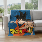 Blaue Dragon Ball Super Kuscheldecke mit großem Son-Goku-Motiv, dekorativ ausgebreitet auf einer grauen Couch in einem hellen Wohnzimmer mit Fensterfront.