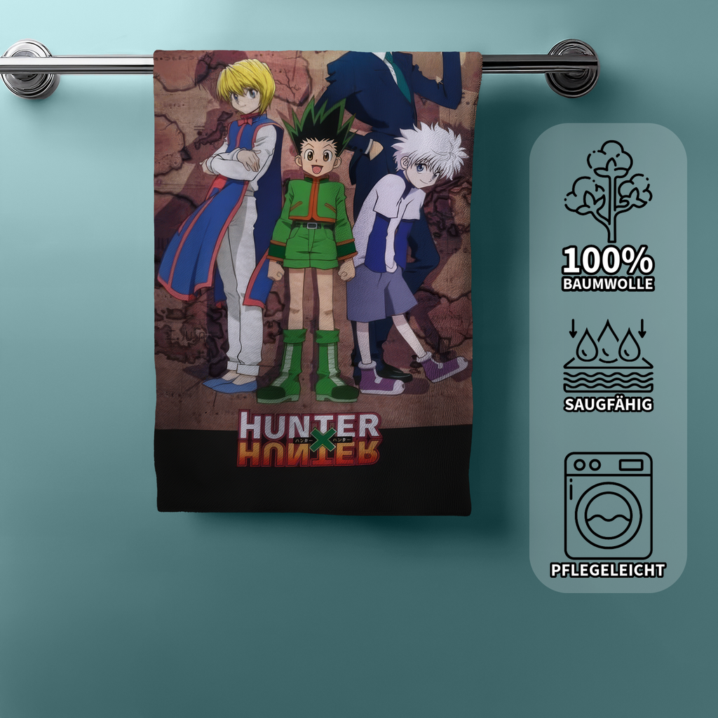 Hunter x Hunter Badetuch an einer Handtuchstange; auf der rechten Seite zeigen drei Icons die Eigenschaften „100% Baumwolle“, „Saugfähig“ und „Pflegeleicht“.
