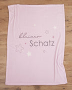 Rosa Babydecke ausgebreitet auf Holzboden mit dem vollständigen Motiv aus Sternen und dem Schriftzug „kleiner Schatz“.