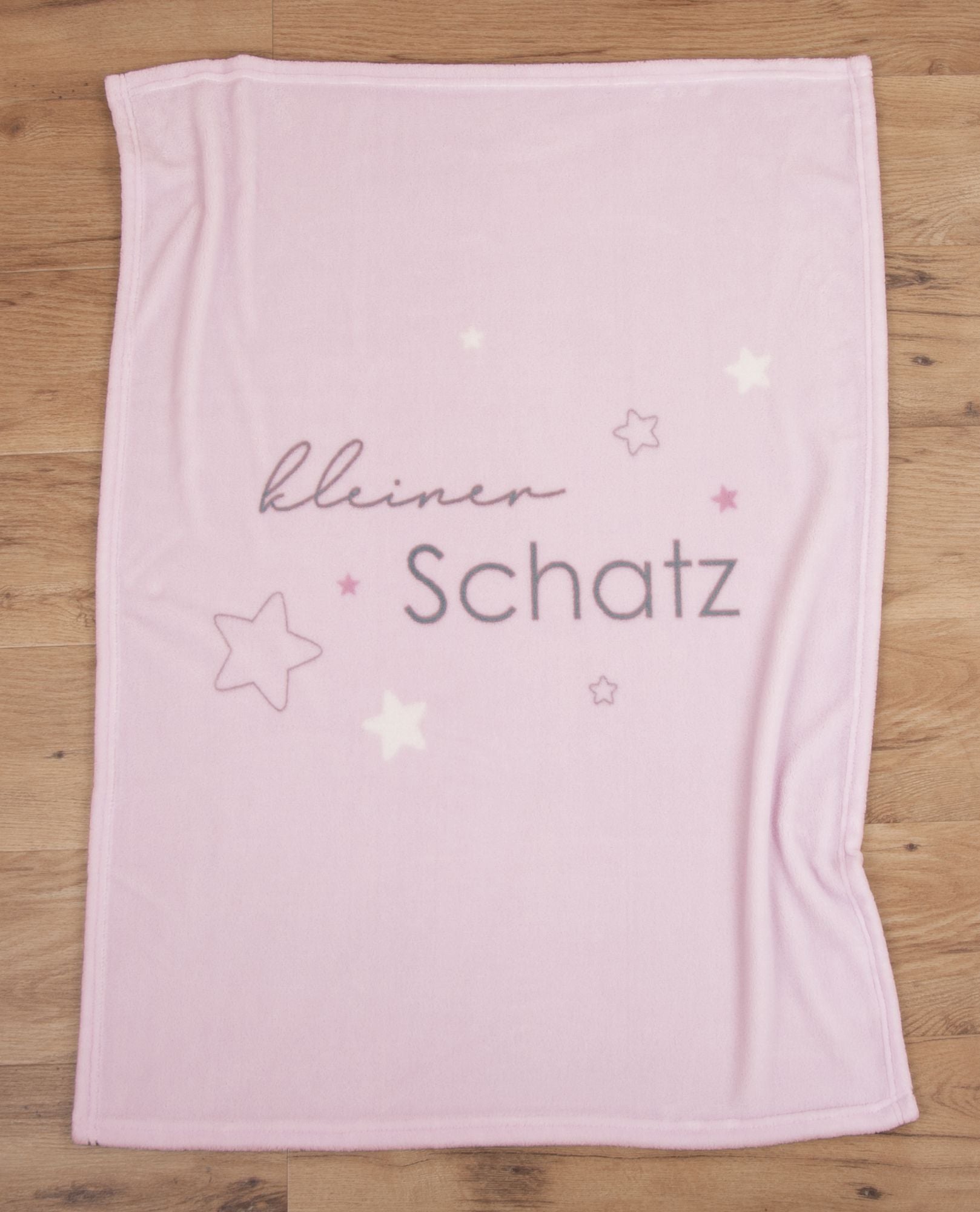 Rosa Babydecke ausgebreitet auf Holzboden mit dem vollständigen Motiv aus Sternen und dem Schriftzug „kleiner Schatz“.