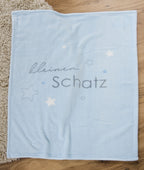 Hellblaue Babydecke komplett ausgebreitet auf Holzboden; zeigt das vollständige Motiv mit Sternen und Text.