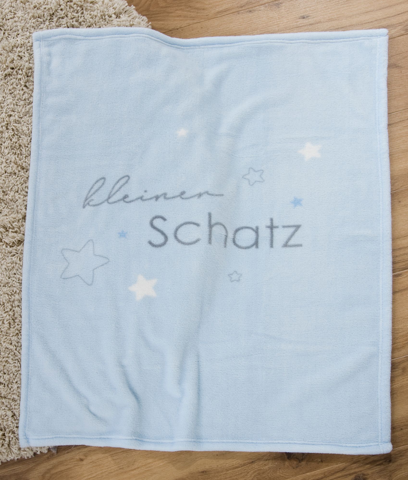 Hellblaue Babydecke komplett ausgebreitet auf Holzboden; zeigt das vollständige Motiv mit Sternen und Text.