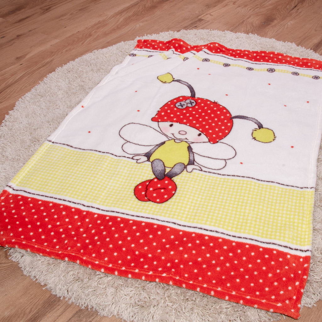 Die Baby-Kuscheldecke liegt ausgebreitet auf einem runden Teppich vor Holzfußboden. Das Motiv zeigt ein sitzendes Käferchen-Mädchen mit Flügeln über einem grün-weiß karierten Streifen und einem roten Punktemuster.