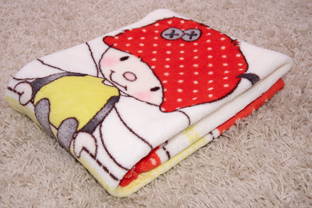 Zusammengelegte Baby-Kuscheldecke auf einem hellen, zotteligen Teppich; zu sehen ist ein Ausschnitt des aufgedruckten Motivs mit einem niedlichen Käferchen, das eine rote Mütze mit weißen Punkten trägt.