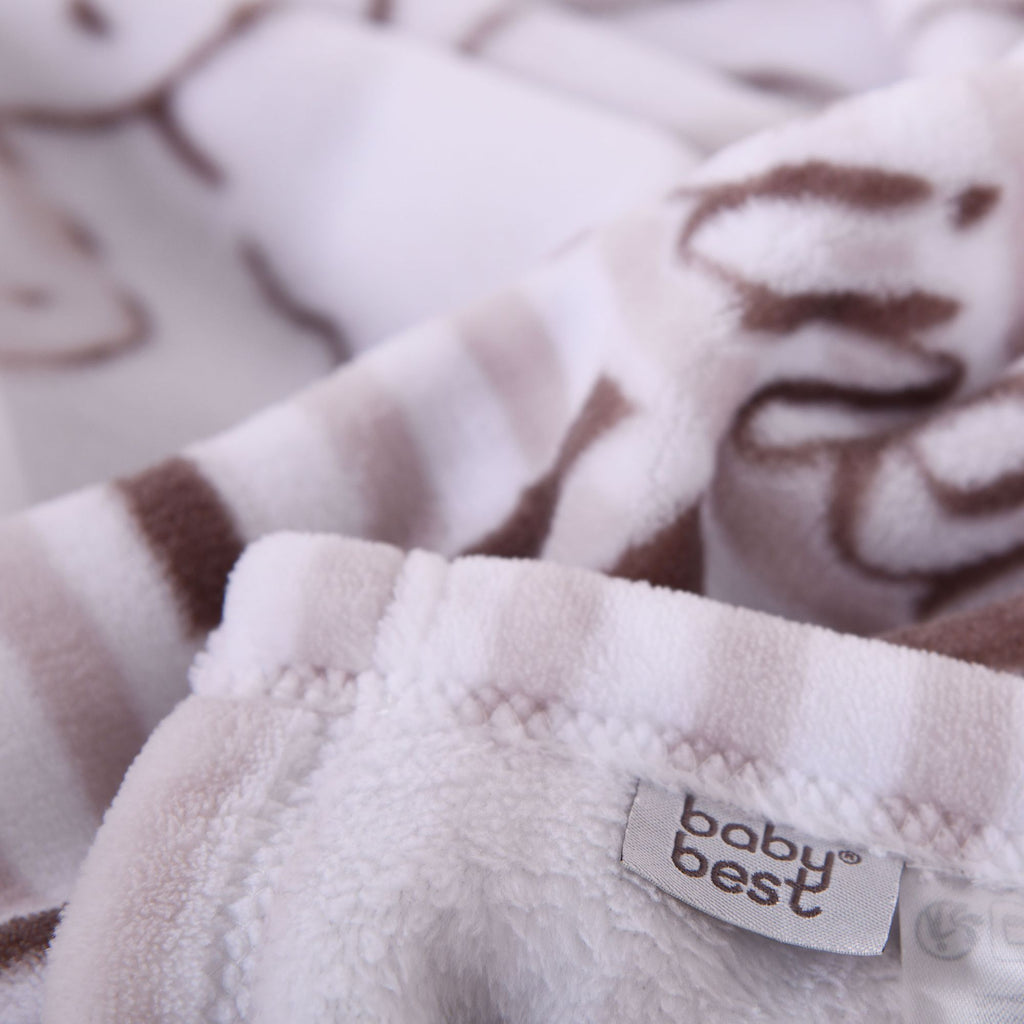 Nahaufnahme des weichen, flauschigen Materials der Kuscheldecke; im Fokus stehen der sauber verarbeitete Rand und das eingenähte „baby best“-Markenlabel vor gestreiftem Hintergrund.
