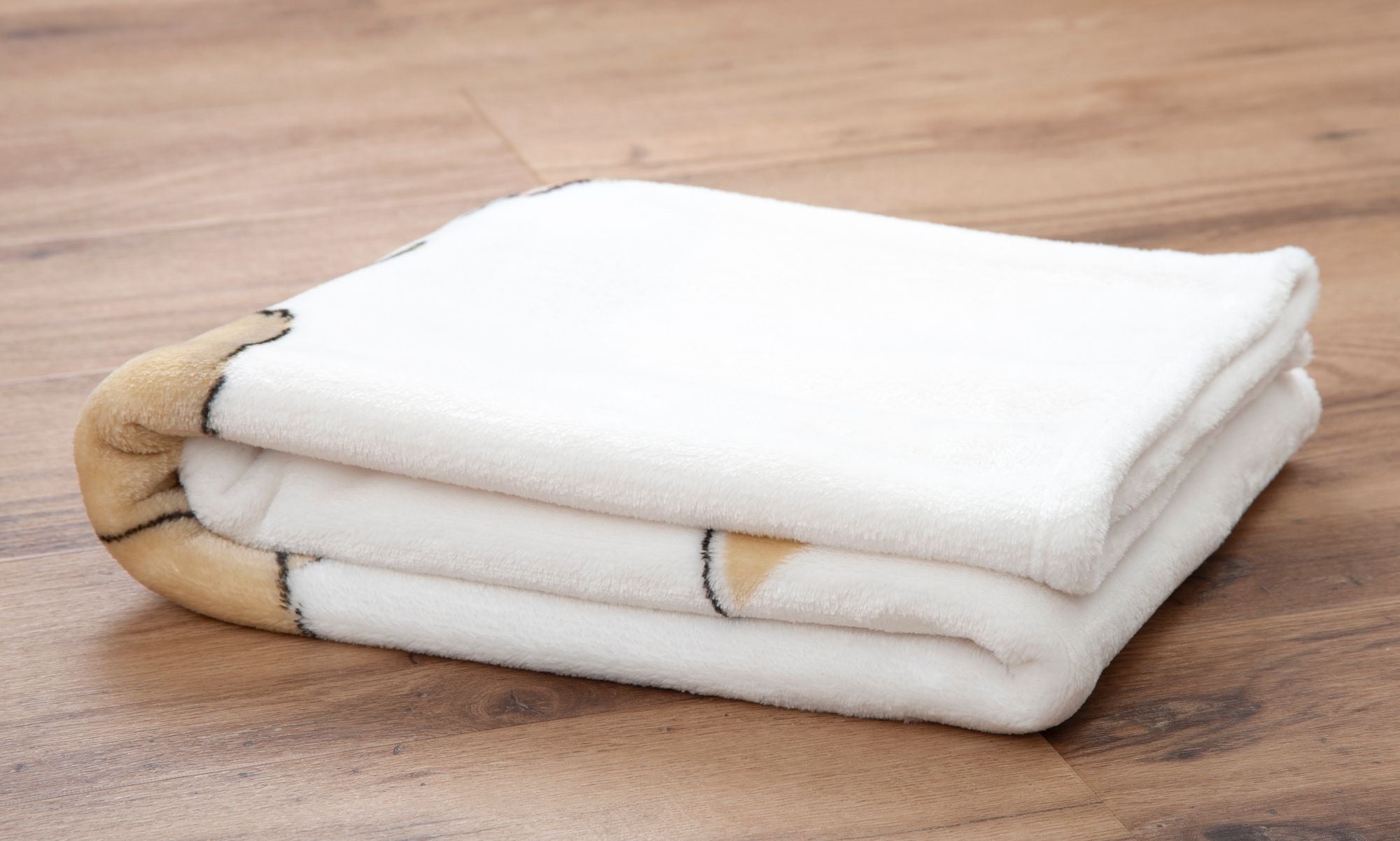 Die Decke liegt dreifach gefaltet auf einem Holzuntergrund; diese Rückansicht zeigt das dichte, weiße Flauschmaterial sowie die sauber verarbeiteten, weichen Kanten der Babydecke.