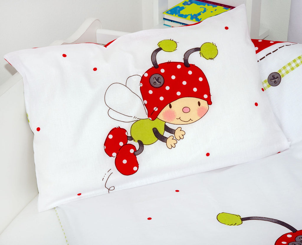 Nahaufnahme des Kopfkissens der Babybettwäsche; im Fokus steht ein fliegender, niedlicher Käfer mit rot-weiß gepunkteter Mütze auf weißem Grund mit roten Punkten.