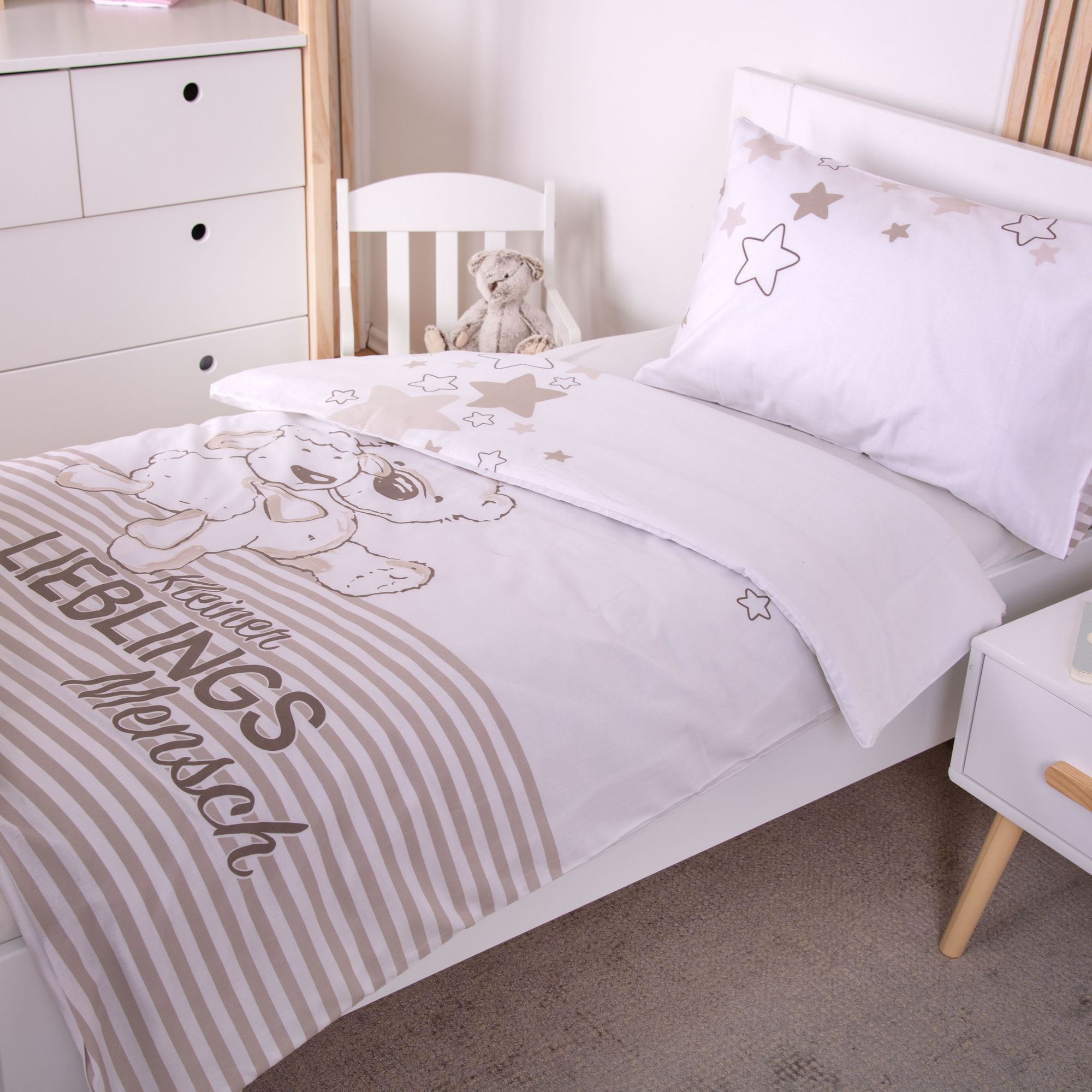 Nahaufnahme der Bettwäsche im Gitterbett von der Seite; zeigt das Hauptmotiv mit einem gezeichneten Bären und Schaf über einem gestreiften Muster mit dem Text „Kleiner LIEBLINGS Mensch“.