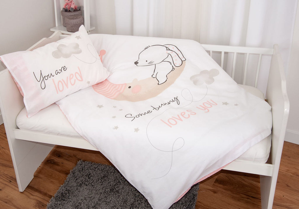 Ambiente-Aufnahme der Babybettwäsche in einem weißen Kinderbett; die Decke ist ausgebreitet und präsentiert das Hasen-Motiv auf weißem Grund, während das Kissen daneben liegt und den Schriftzug „You are loved“ zeigt.