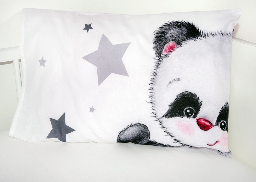 Nahaufnahme eines weißen Babykopfkissens im Gitterbett, das auf der rechten Seite das Gesicht eines süßen Pandas mit rosa Wangen und links ein Muster aus grauen Sternen zeigt.