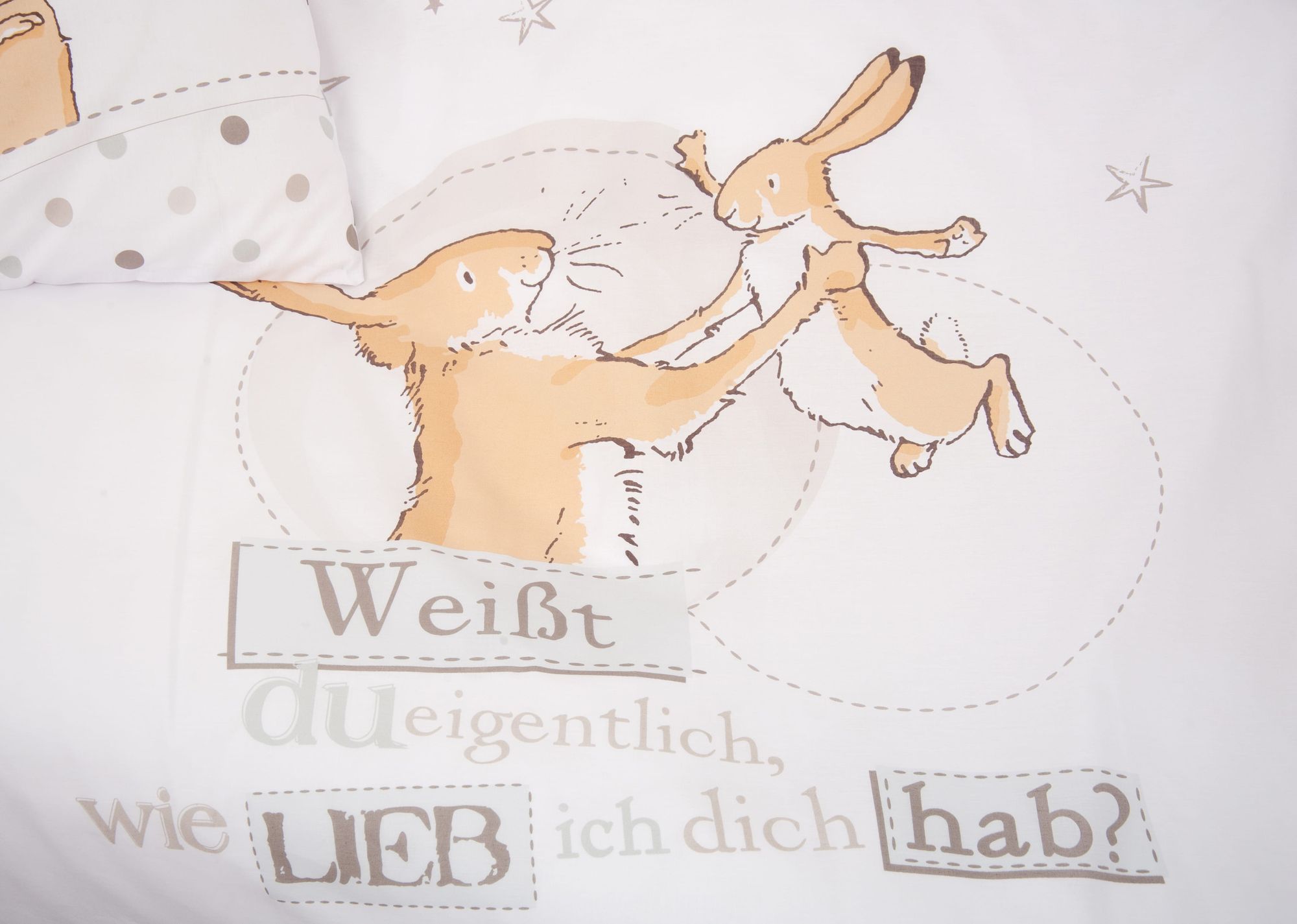 Nahaufnahme der weißen Kinderbettwäsche „Weißt du eigentlich, wie lieb ich dich hab?“; zeigt den großen und den kleinen Hasen beim gemeinsamen Spielen sowie den bekannten Buchtitel als gestalteten Schriftzug.