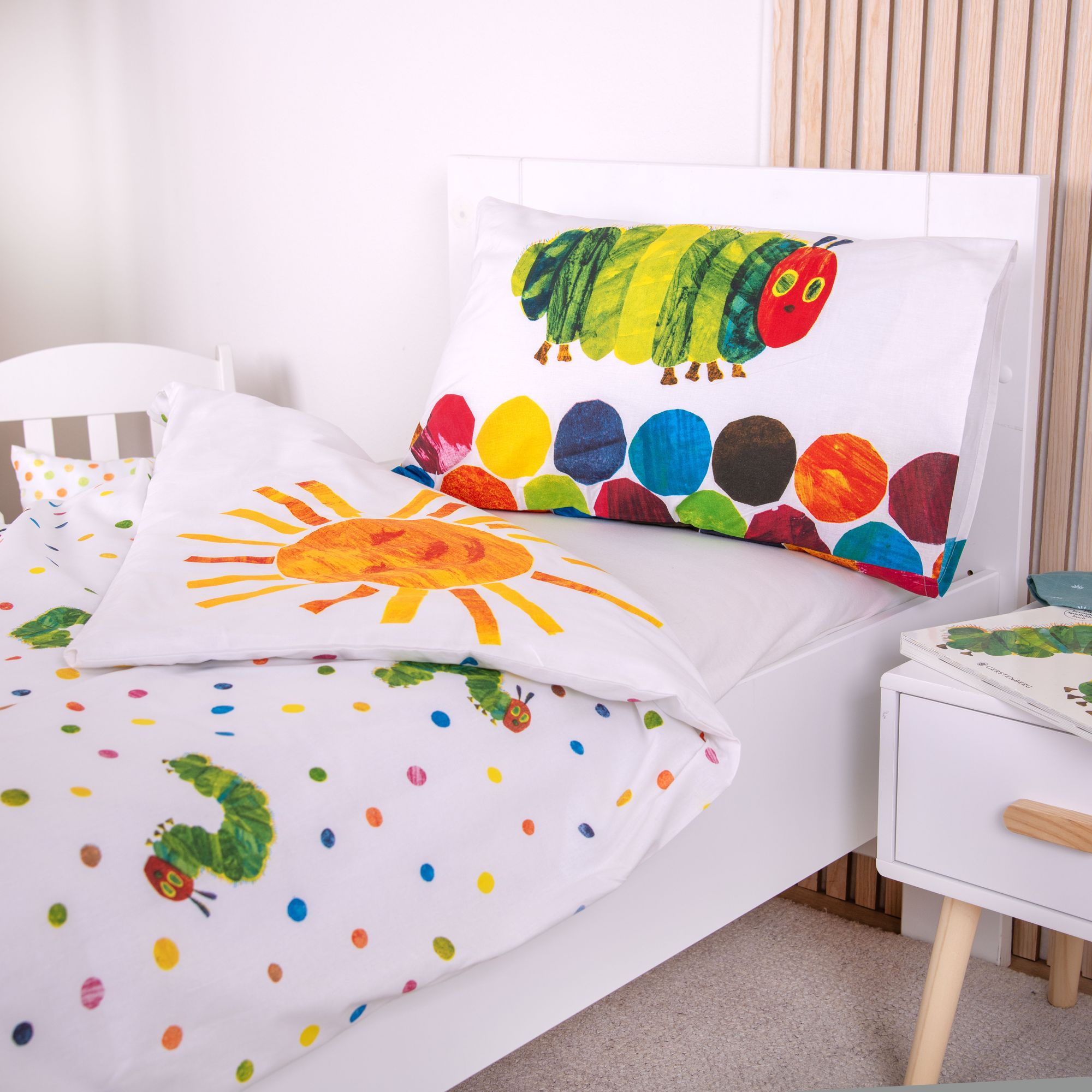 Detaillierte Ambiente-Aufnahme der umgeschlagenen Bettwäsche; veranschaulicht die weiße Rückseite des Deckenbezugs mit farbigen Punkten und kleinen Raupen-Motiven sowie die Kissenrückseite, die ebenfalls die Raupe zeigt.