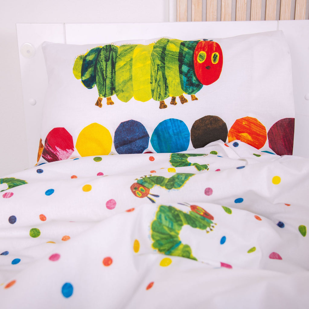 Nahaufnahme des Kopfkissens im Kinderbett; zeigt die große Raupe Nimmersatt auf weißem Grund über einer Reihe aus bunten, gemalten Kreisen.