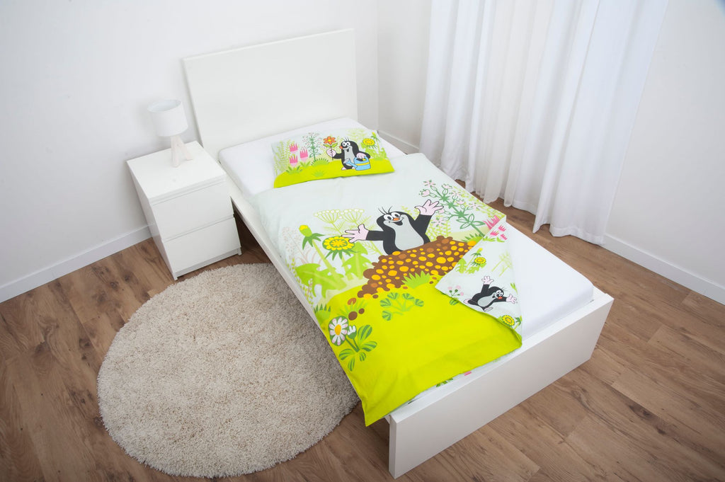 Ambiente-Aufnahme der Kinderbettwäsche „Der kleine Maulwurf“ in einem weißen Bett; der Deckenbezug zeigt den Maulwurf, wie er fröhlich aus seinem Maulwurfshügel auf einer grünen Wiese herausschaut, während das Kopfkissen am Kopfende platziert ist.