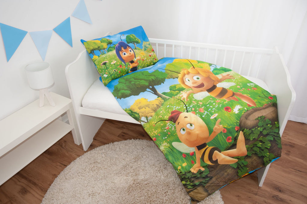 Ambiente-Aufnahme der Kinderbettwäsche „Die Biene Maja“ in einem weißen Bett; die Decke zeigt Maja und Willi fröhlich auf einer grünen Blumenwiese, während das passende Kissen am Kopfende liegt.
