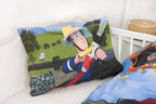 Nahaufnahme des Kopfkissens im Kinderbett; zeigt Feuerwehrmann Sam im Einsatz mit einem Feuerwehrschlauch beim Löschen vor einer ländlichen Kulisse.