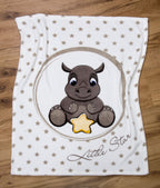Ambiente-Aufnahme der Kuscheldecke flach ausgebreitet auf hellem Holzboden; zeigt das sitzende Nashorn-Baby mit gelbem Stern im Kreis und den Schriftzug „Little Star“ inmitten eines Sternenmusters.