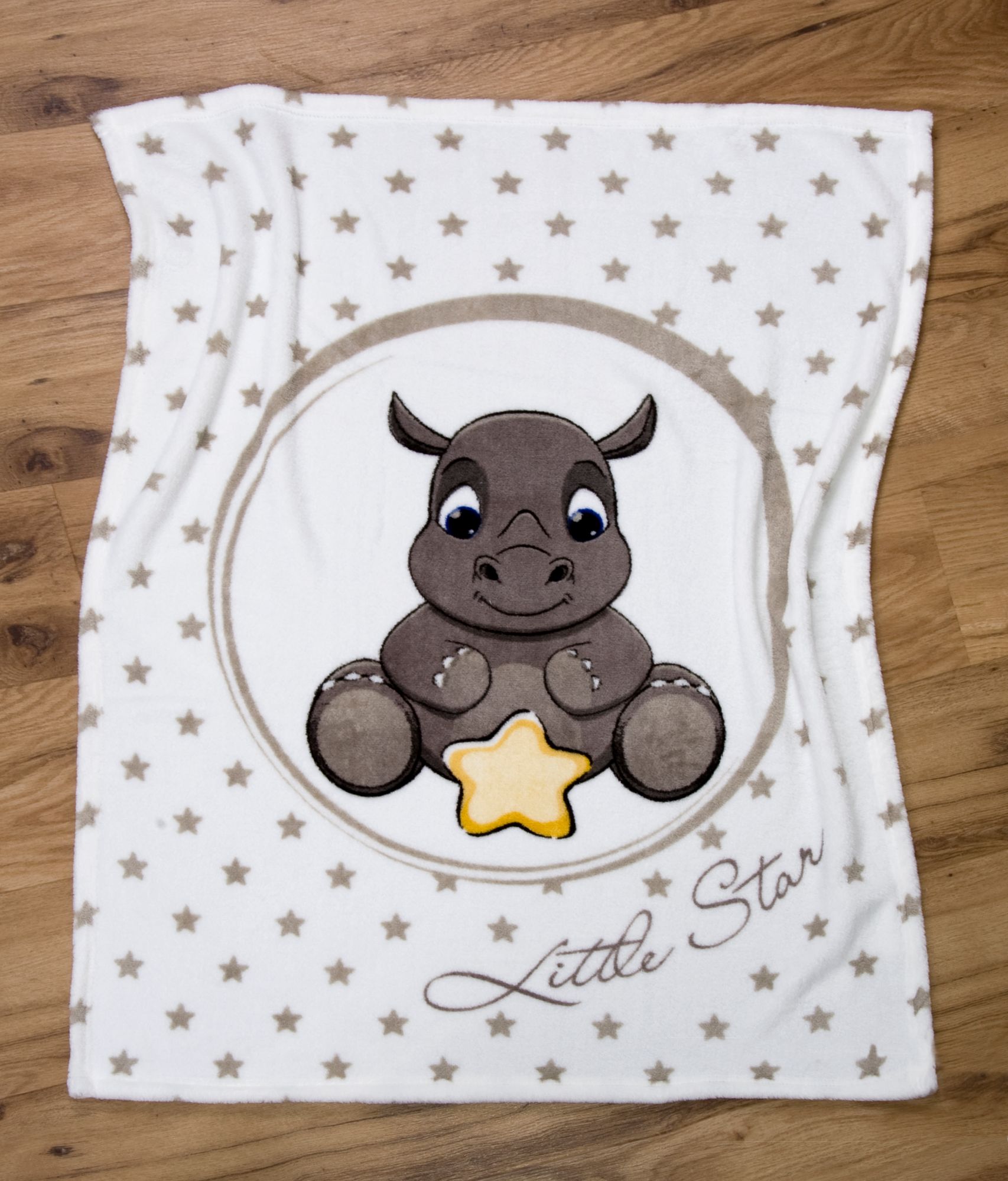 Ambiente-Aufnahme der Kuscheldecke flach ausgebreitet auf hellem Holzboden; zeigt das sitzende Nashorn-Baby mit gelbem Stern im Kreis und den Schriftzug „Little Star“ inmitten eines Sternenmusters.
