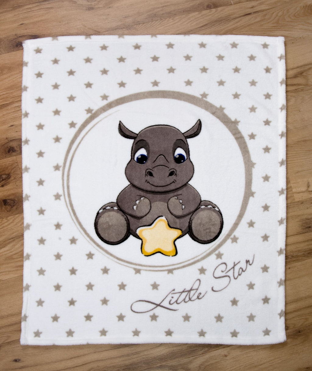 Draufsicht der Babydecke flach ausgebreitet auf hellem Holzboden; zeigt die gesamte Vorderseite mit dem Nashorn-Motiv und dem Sternen-Hintergrund in einer zentrierten, geraden Ansicht.