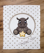 Draufsicht der Babydecke flach ausgebreitet auf hellem Holzboden; zeigt die gesamte Vorderseite mit dem Nashorn-Motiv und dem Sternen-Hintergrund in einer zentrierten, geraden Ansicht.